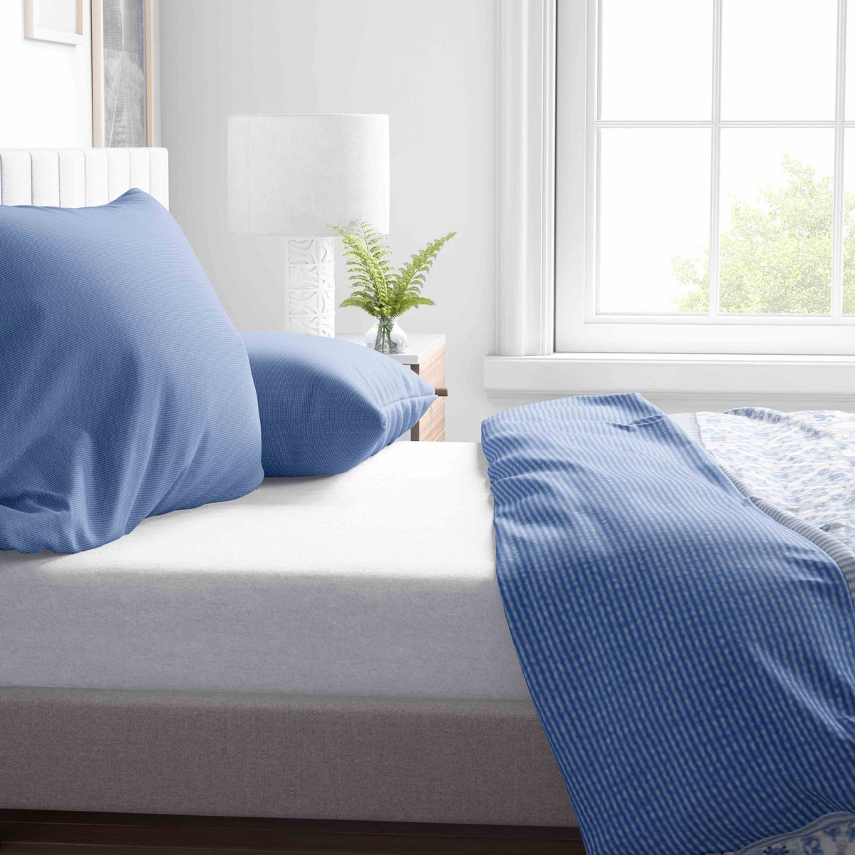 <img src="2.jpg" alt="Nahaufnahme von blauem Kopfkissenbezug und Bettdecke mit Streifenmuster, arrangiert auf einem Bett neben einem Nachttisch mit Pflanze">