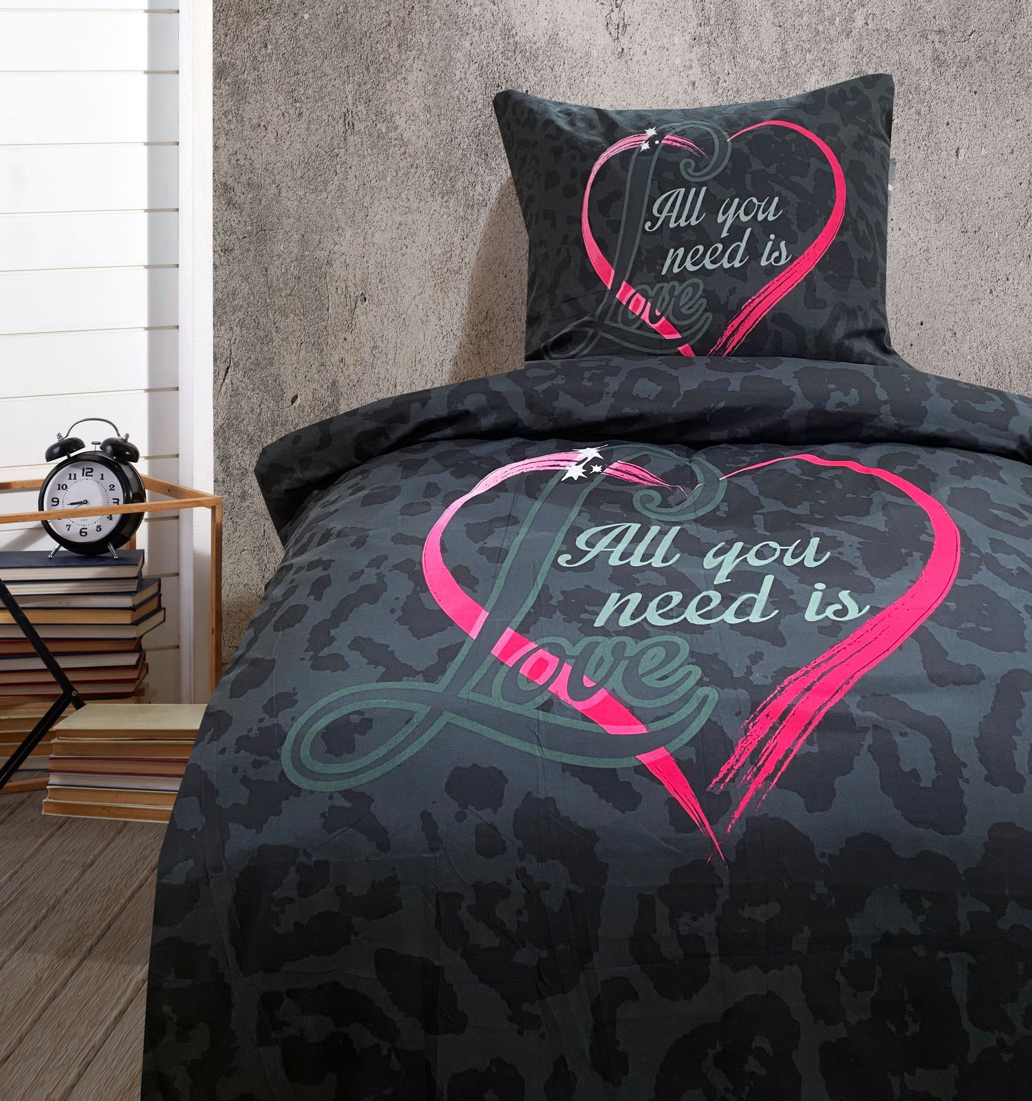 Bettwäsche-Set in Schwarz mit romantischem Herzmotiv „All You Need Is Love“ auf einem gemachten Bett im Schlafzimmer mit Bücherstapel und Wecker